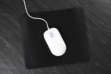 Photo of White wired mouse and mousepad on black textured table, top view