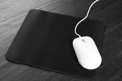 White wired mouse and mousepad on black textured table