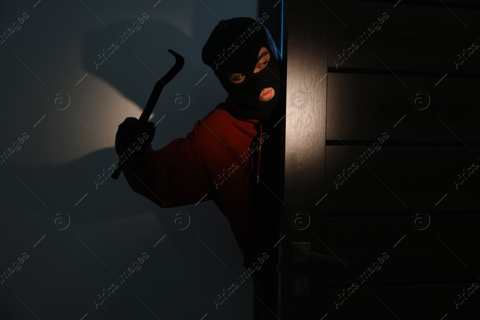 Photo of Thief with crowbar entering foreign house at night. Burglary