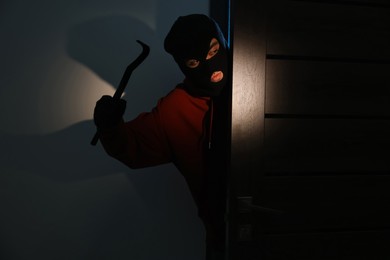 Photo of Thief with crowbar entering foreign house at night. Burglary