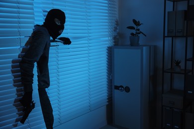 Thief with gun coming out of blinds at night. Burglary