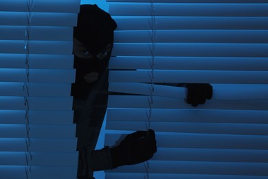 Thief looking out of blinds at night. Burglary