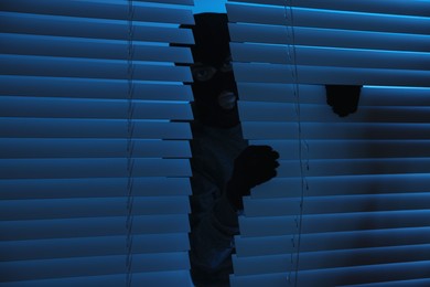 Photo of Thief looking out of blinds at night. Burglary