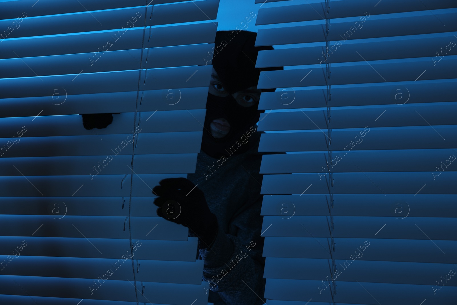 Photo of Thief looking out of blinds at night. Burglary