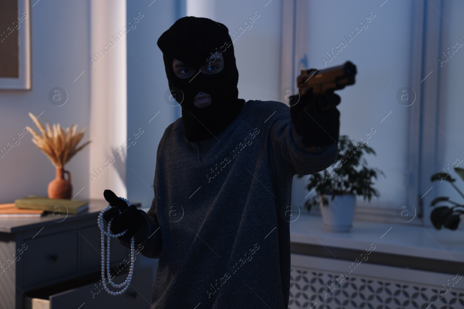 Photo of Thief with gun stealing jewels in foreign house. Burglary