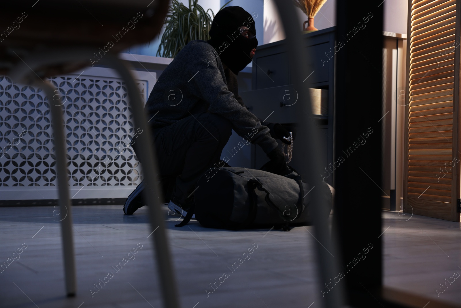 Photo of Thief wearing balaclava stealing jewels in foreign house. Burglary