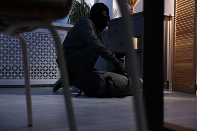 Thief wearing balaclava stealing jewels in foreign house. Burglary