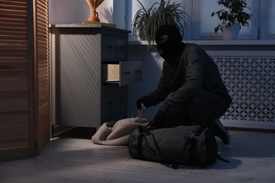 Photo of Thief wearing balaclava stealing jewels in foreign house. Burglary