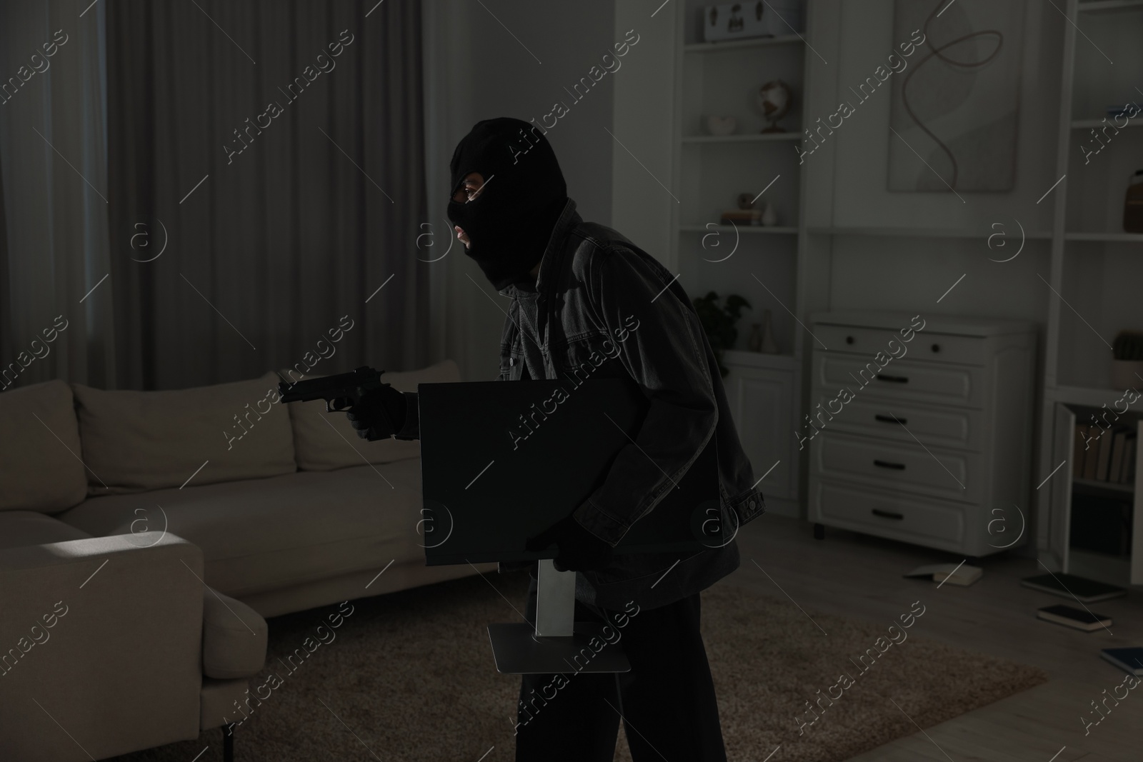 Photo of Thief with gun stealing computer monitor at foreign house. Burglary