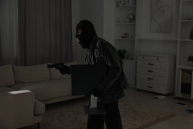 Photo of Thief with gun stealing computer monitor at foreign house. Burglary