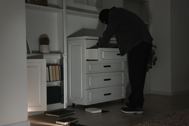 Thief looking for money in chest of drawers at foreign house. Burglary