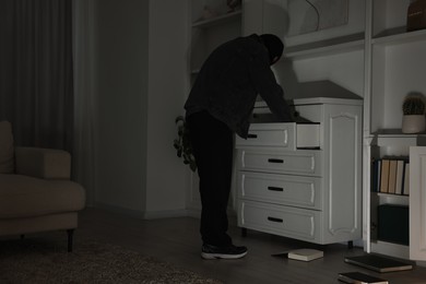 Photo of Thief looking for money in chest of drawers at foreign house. Burglary