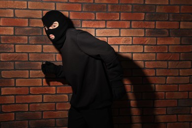 Photo of Thief in balaclava against red brick wall