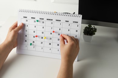 Photo of Timetable. Man marking date in calendar with drawing pins at white table, closeup