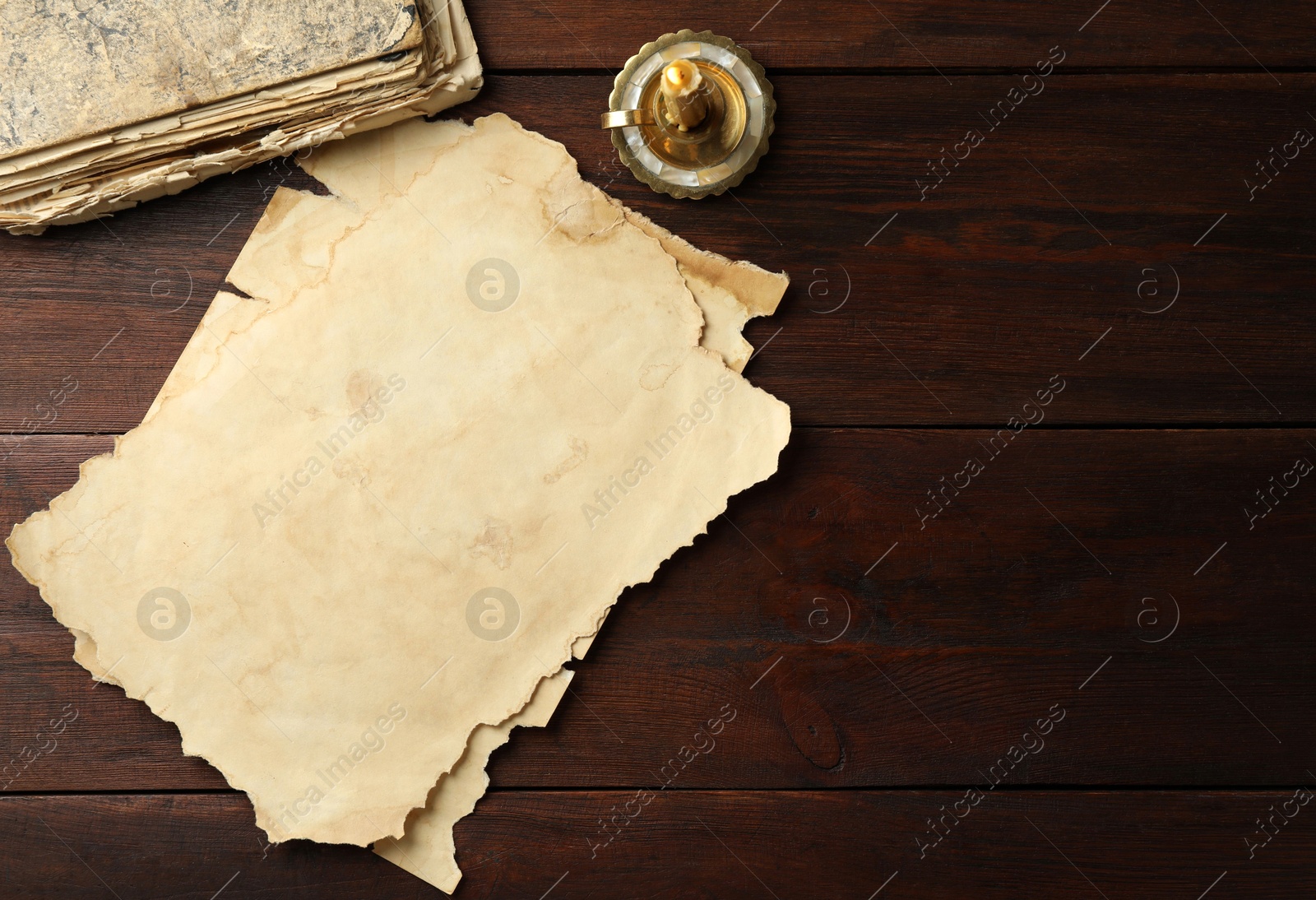 Photo of Sheets of old parchment paper, vintage book and candle on wooden table, flat lay. Space for text