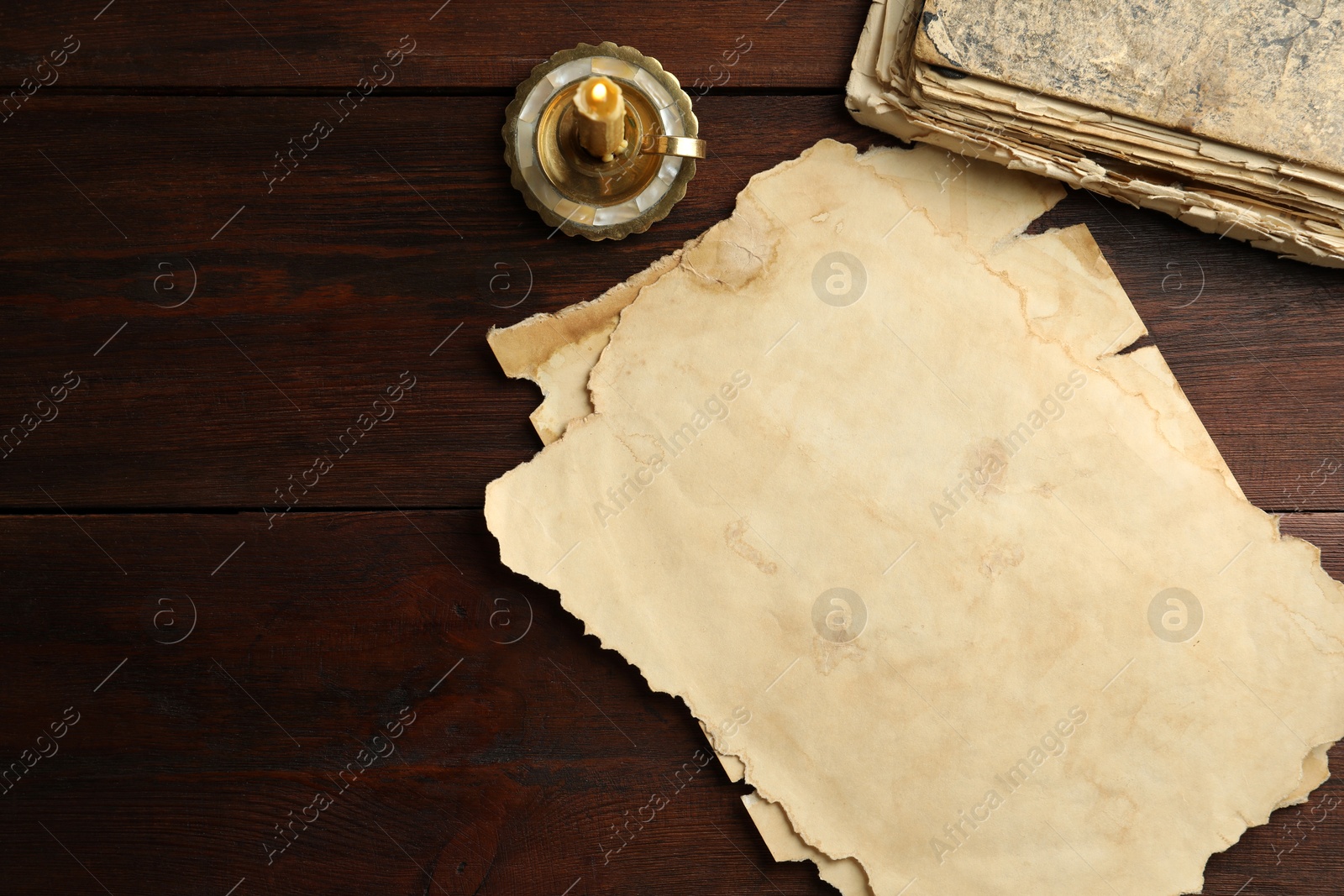 Photo of Sheets of old parchment paper, vintage book and candle on wooden table, flat lay. Space for text