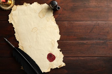 Sheet of old parchment paper with wax stamp, black feather, inkwell and candle on wooden table, flat lay. Space for text