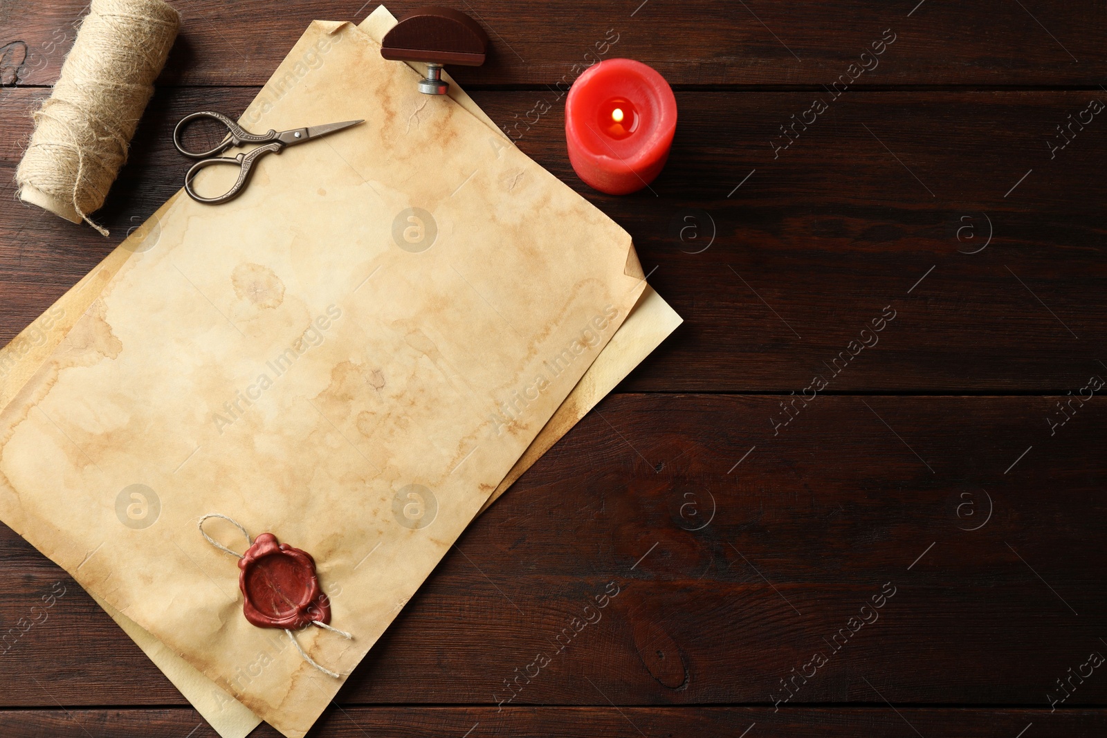 Photo of Sheet of old parchment paper with wax stamp, rope, scissors and candle on wooden table, flat lay