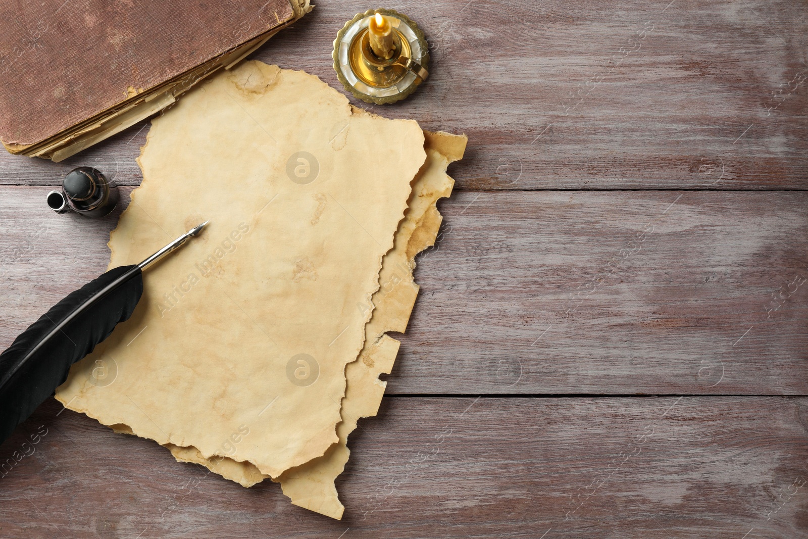 Photo of Sheet of old parchment paper, black feather, inkwell, vintage book and candle on wooden table, flat lay. Space for text