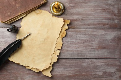 Sheet of old parchment paper, black feather, inkwell, vintage book and candle on wooden table, flat lay. Space for text