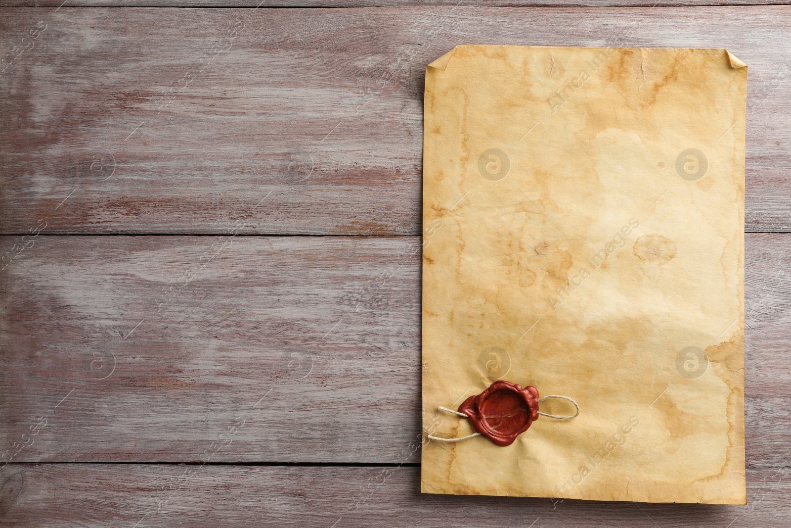 Photo of Sheet of old parchment paper with wax stamp on wooden table, top view. Space for text