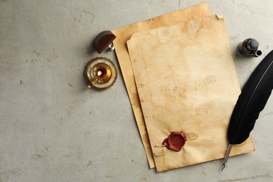 Photo of Sheet of old parchment paper with wax stamp, black feather, inkwell and candle on grey table, flat lay. Space for text