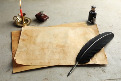 Sheet of old parchment paper, black feather, inkwell and candle on grey table