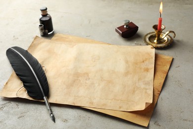 Sheet of old parchment paper, black feather, inkwell and candle on grey table