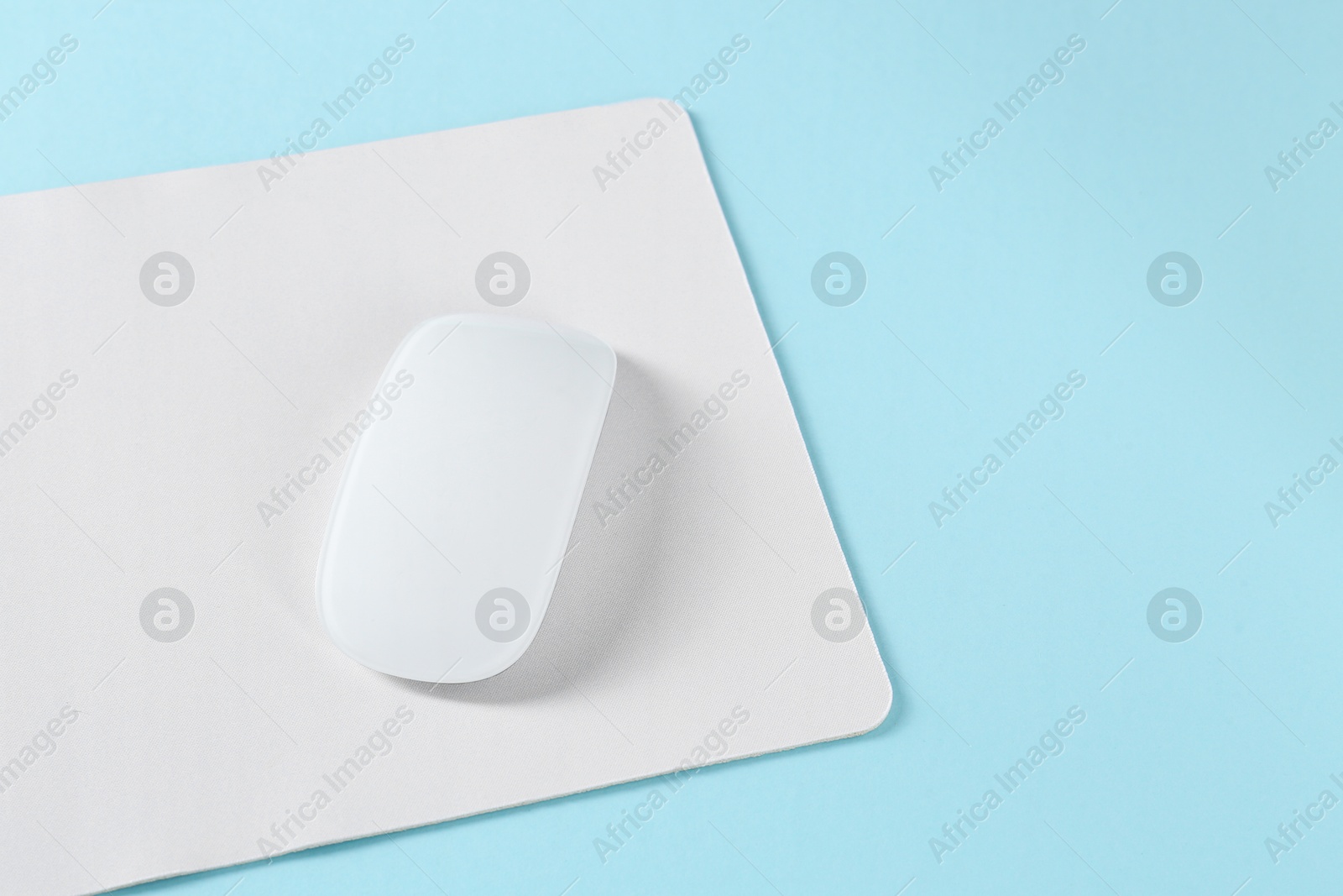 Photo of Wireless mouse and mousepad on light blue background, space for text