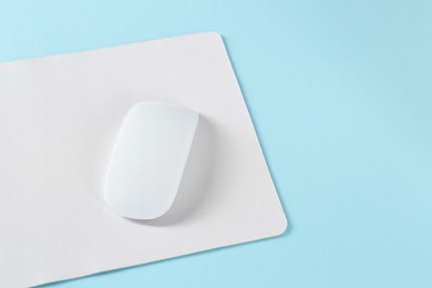 Photo of Wireless mouse and mousepad on light blue background, space for text