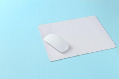 Wireless mouse and mousepad on light blue background, space for text