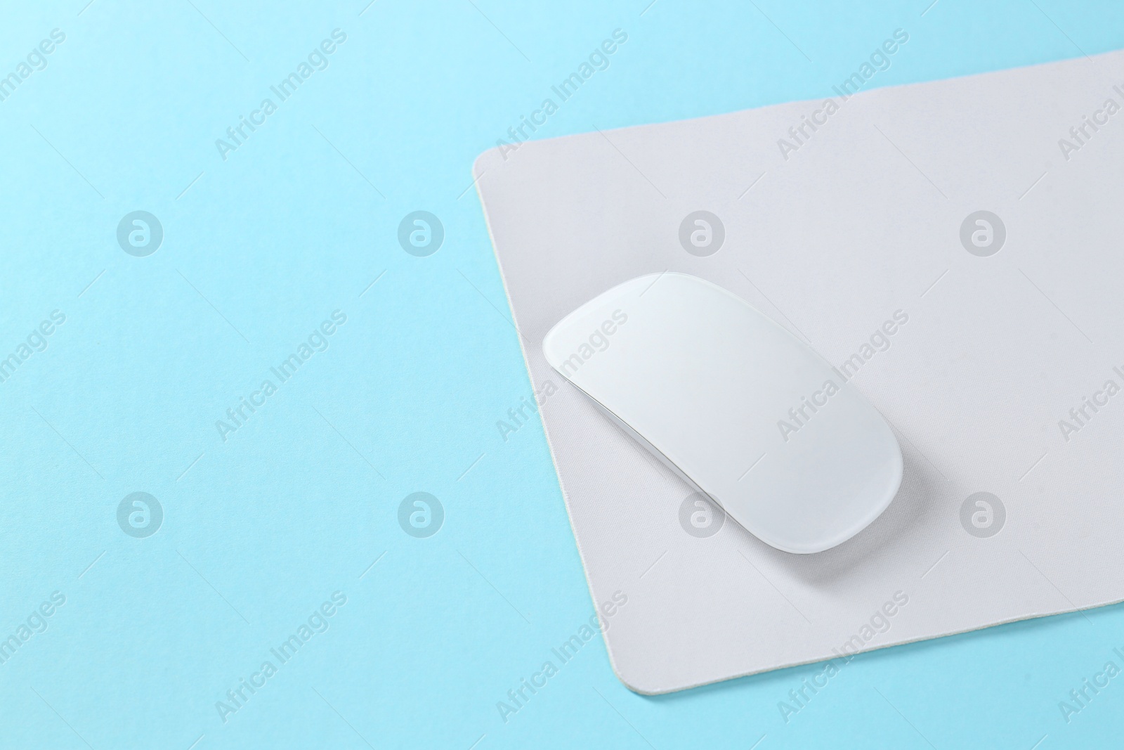 Photo of Wireless mouse and mousepad on light blue background, space for text