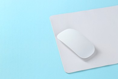 Wireless mouse and mousepad on light blue background, space for text