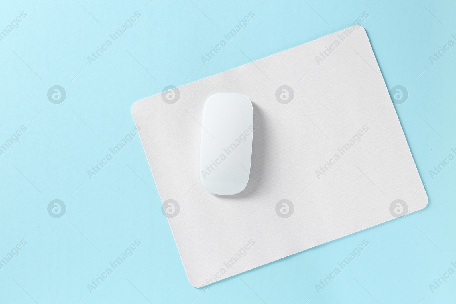 Photo of Wireless mouse and mousepad on light blue background, top view. Space for text