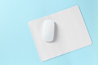 Wireless mouse and mousepad on light blue background, top view. Space for text