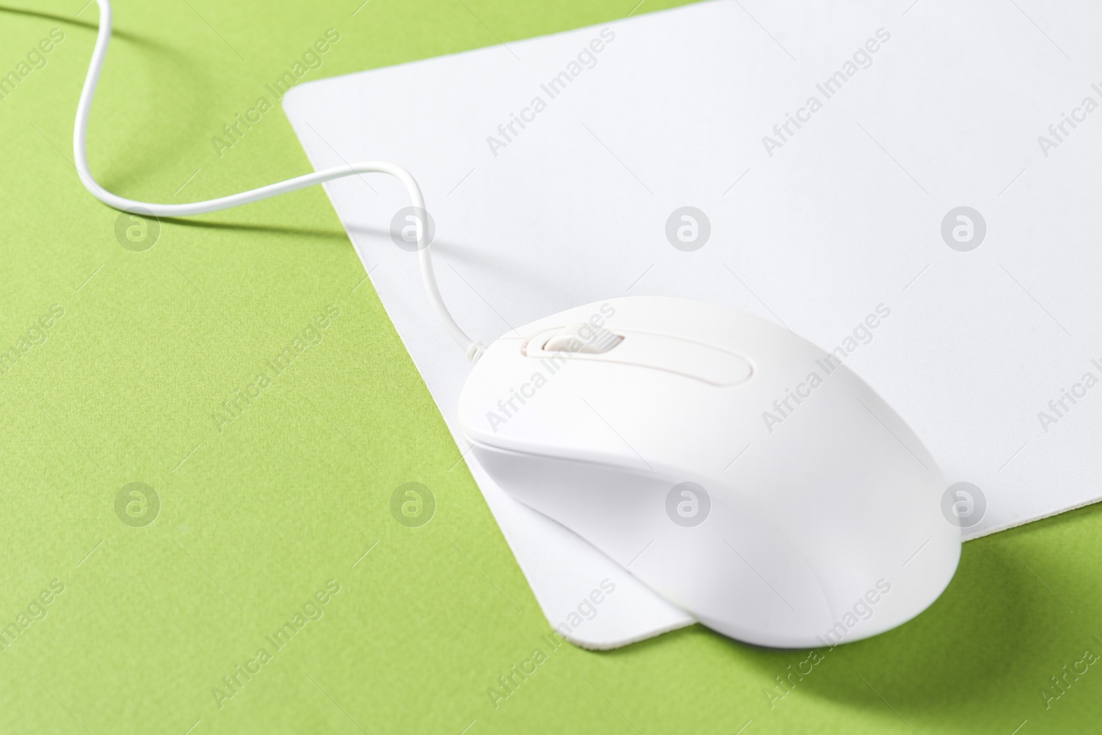 Photo of Wired mouse and mousepad on green background, space for text