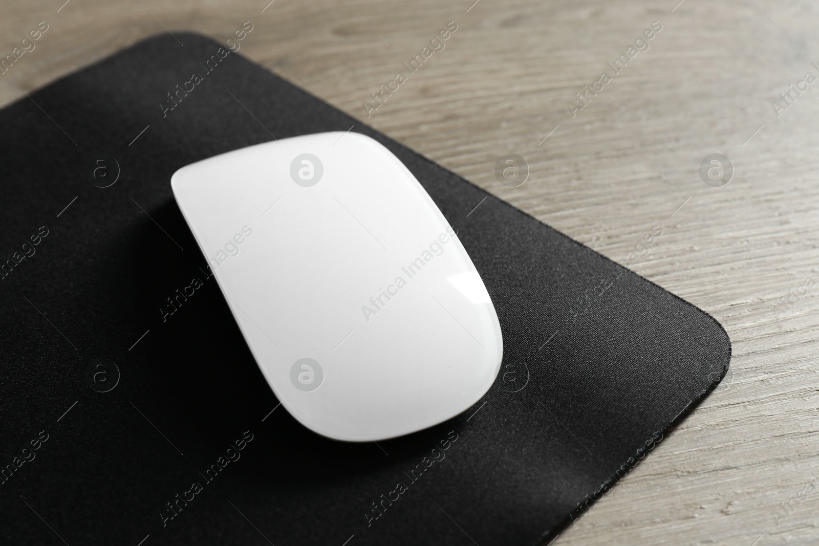 Photo of Wireless mouse and mousepad on wooden table, closeup