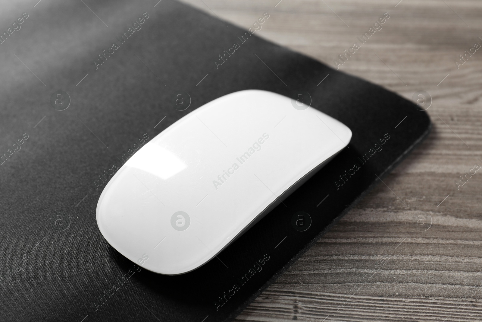 Photo of Wireless mouse and mousepad on wooden table, closeup