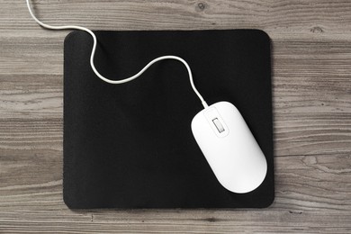 Wired mouse and mousepad on wooden table, top view