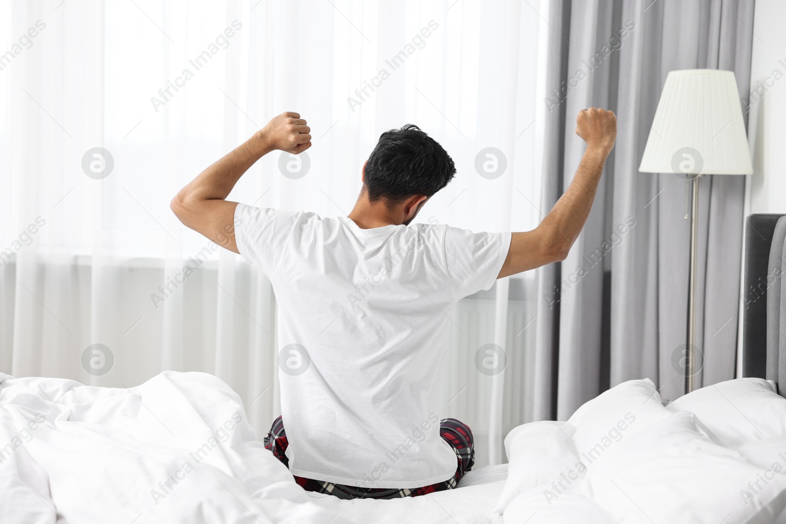 Photo of Good morning. Man stretching on bed at home, back view