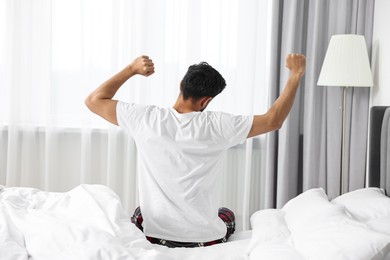 Good morning. Man stretching on bed at home, back view