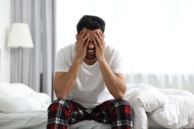 Tired man covering face with hands on bed at morning