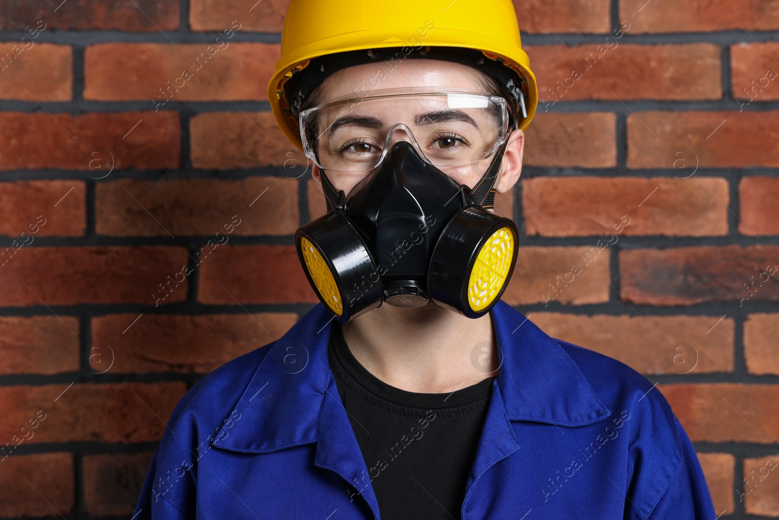 Photo of Worker in respirator, protective glasses and helmet near brick wall