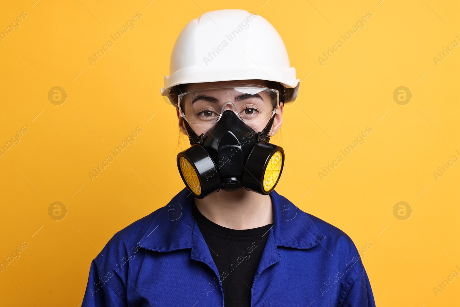 Photo of Worker in respirator, protective glasses and helmet on orange background