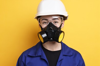 Photo of Worker in respirator, protective glasses and helmet on orange background