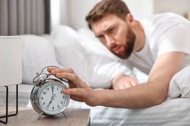 Photo of Sleepy young man turning off alarm clock in bedroom at morning, selective focus