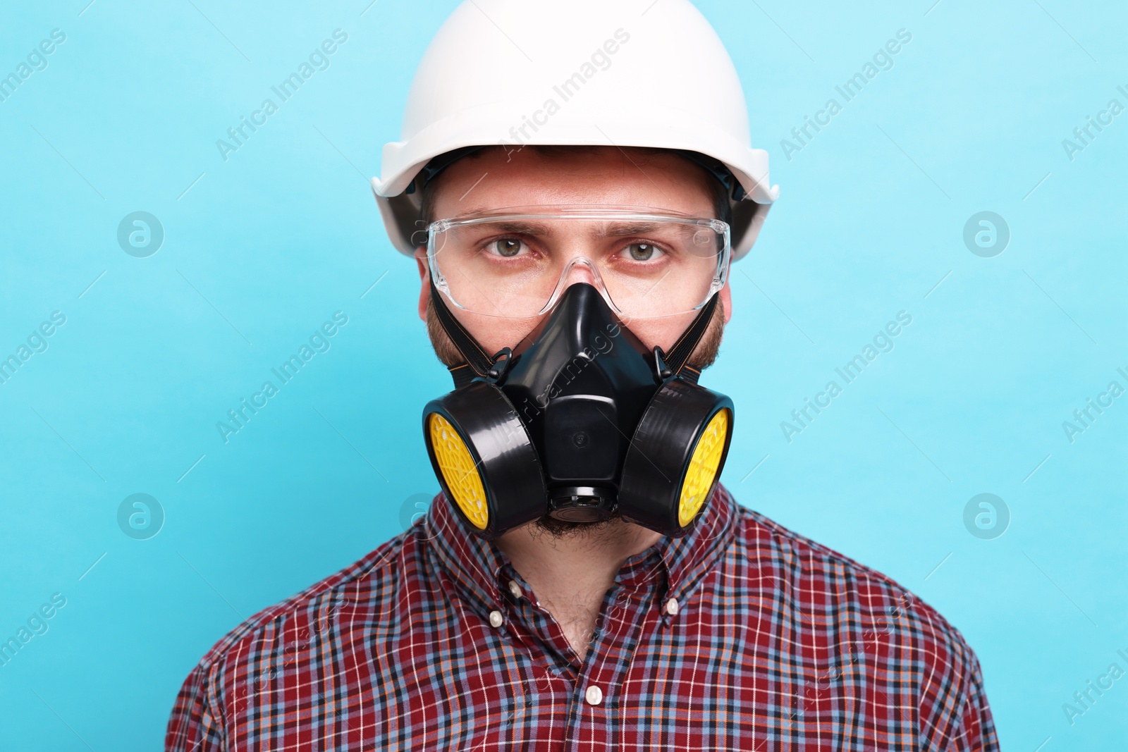 Photo of Man in respirator mask and hard hat on light blue background