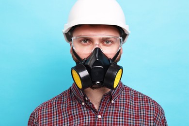 Man in respirator mask and hard hat on light blue background