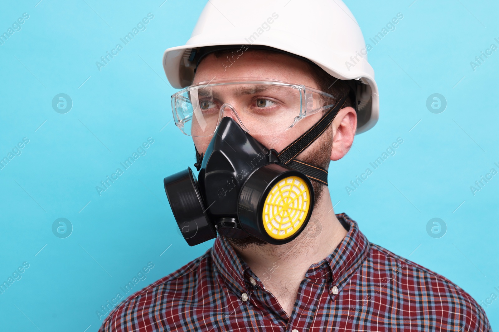 Photo of Man in respirator mask and hard hat on light blue background