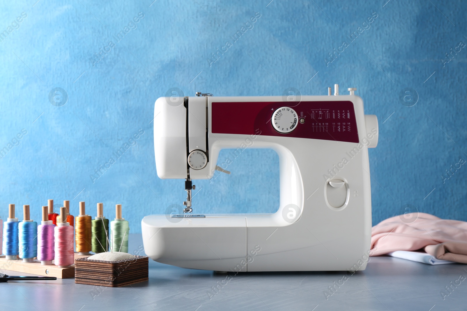 Photo of White sewing machine and craft accessories on gray table near light blue wall